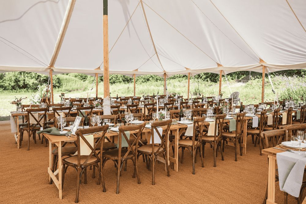 Long banquet tables with oak cross-back chairs set inside a traditional marquee on coir matting
