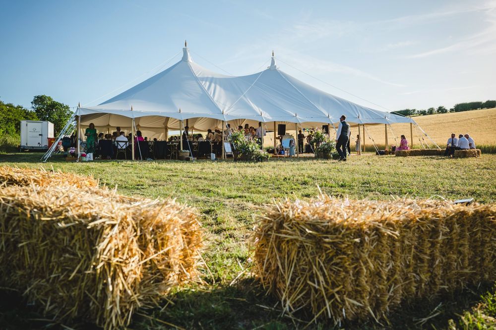 A traditional pole marquee in a countryside field with straw bales set out as seating