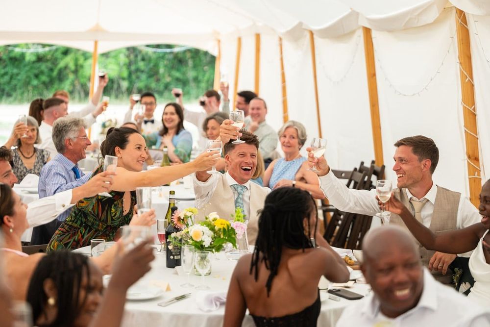 Wedding guests raising a toast at a table inside a marquee with clear sidewalls